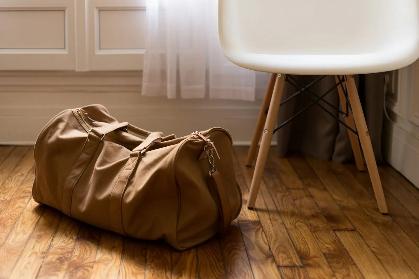 Brown duffel bag beside a wooden chair