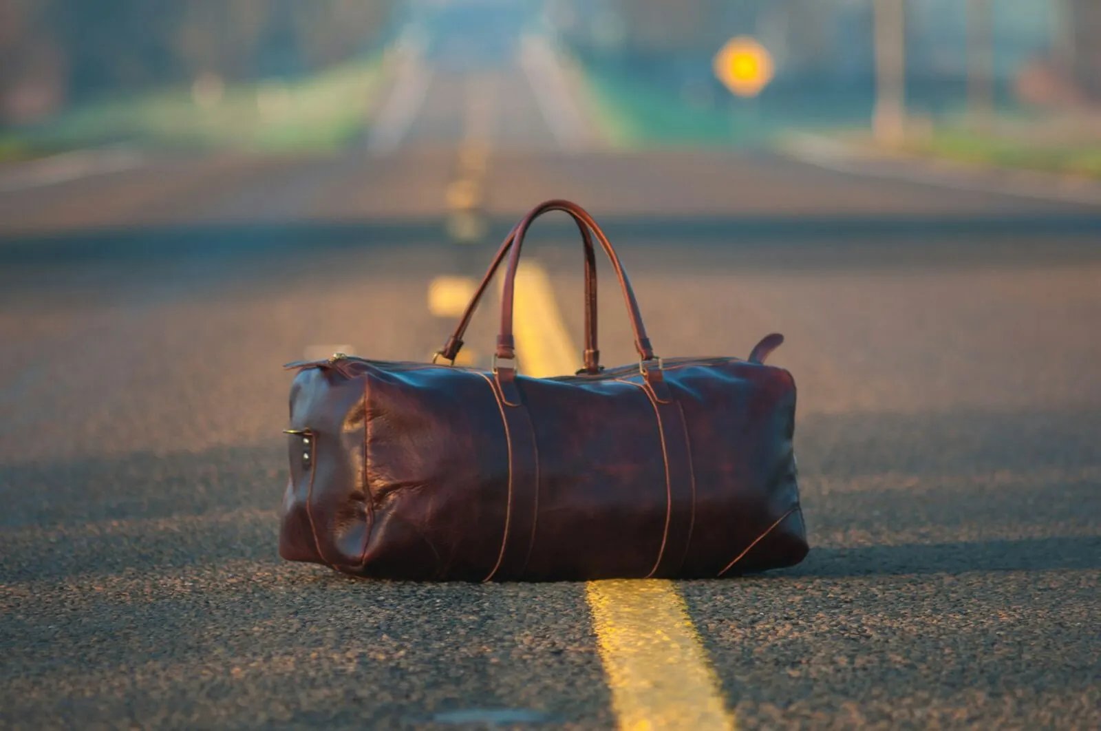 Brown leather duffel bag set down on a road